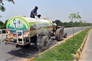 A worker sprays water on roadside greenbelt plants from a tanker along a highway as part of efforts to maintain greenery amid rising temperatures.