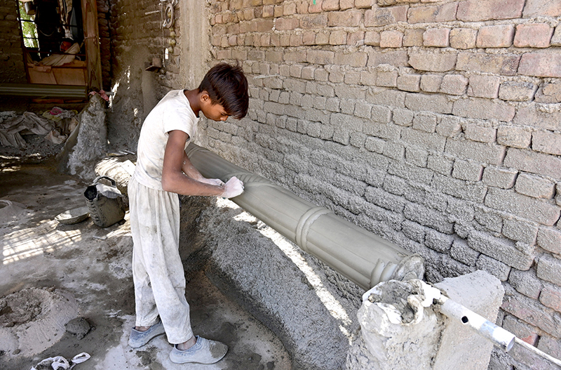 A labourer applies decorative designs to a cement pillar at his roadside workplace area