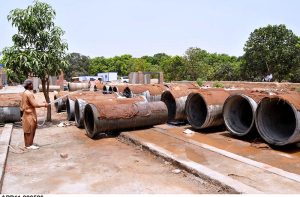 A labourer showers water on a newly built cement sewage manhole pipes at a construction site.