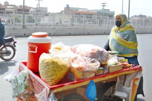 A woman pushes a handcart loaded with snack items for sale along a city road to earn livelihood