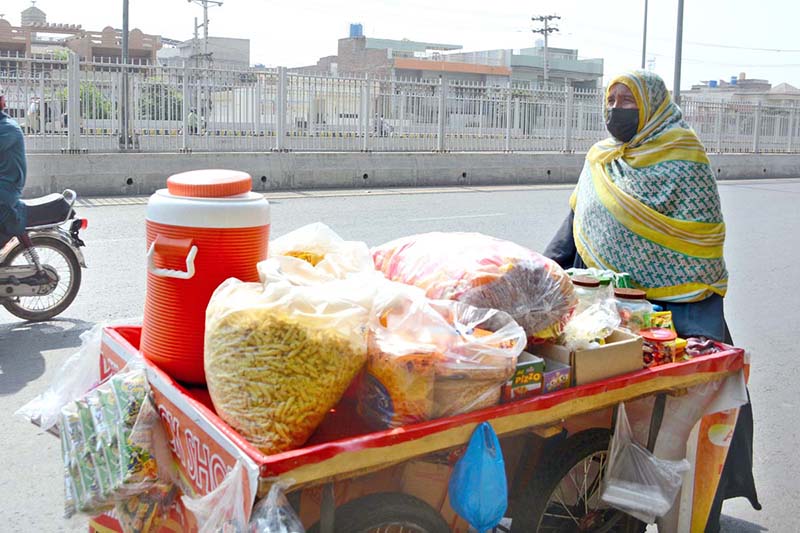 A woman pushes a handcart loaded with snack items for sale along a city road to earn livelihood