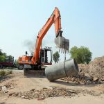 Workers operate heavy machinery while laying the main sewerage pipeline for an underground drainage project in the city