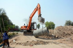 Workers operate heavy machinery while laying the main sewerage pipeline for an underground drainage project in the city