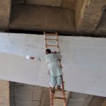 A worker paints a flyover while using a long ladder without proper safety measures during ongoing maintenance work in the city