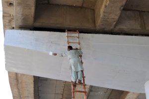 A worker paints a flyover while using a long ladder without proper safety measures during ongoing maintenance work in the city