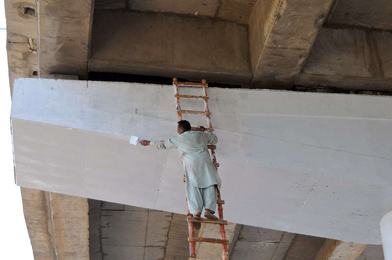 A worker paints a flyover while using a long ladder without proper safety measures during ongoing maintenance work in the city