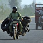 A worker carrying used tyres on a motorcycle after collecting them from different parts of the city for repair and recycling into reusable tyres