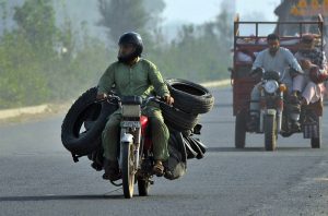 A worker carrying used tyres on a motorcycle after collecting them from different parts of the city for repair and recycling into reusable tyres