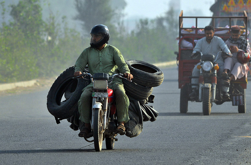 A worker carrying used tyres on a motorcycle after collecting them from different parts of the city for repair and recycling into reusable tyres