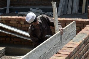 A construction worker uses a hammer to align structural supports on a masonry wall with wooden planks.