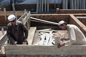 A construction worker uses a hammer to align structural supports on a masonry wall with wooden planks.