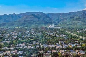 An aerial view of residential areas of Islamabad with the iconic Faisal Masjid nestled against the lush green Margalla Hills in the background.