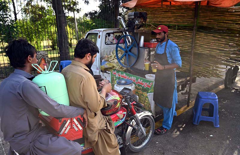 A vendor serves sugarcane juice to customers on a hot day in the city at Stadium Road