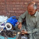 An artisan sits on the Mall Road footpath, repairing eyeglass frames to earn a livelihood for his children