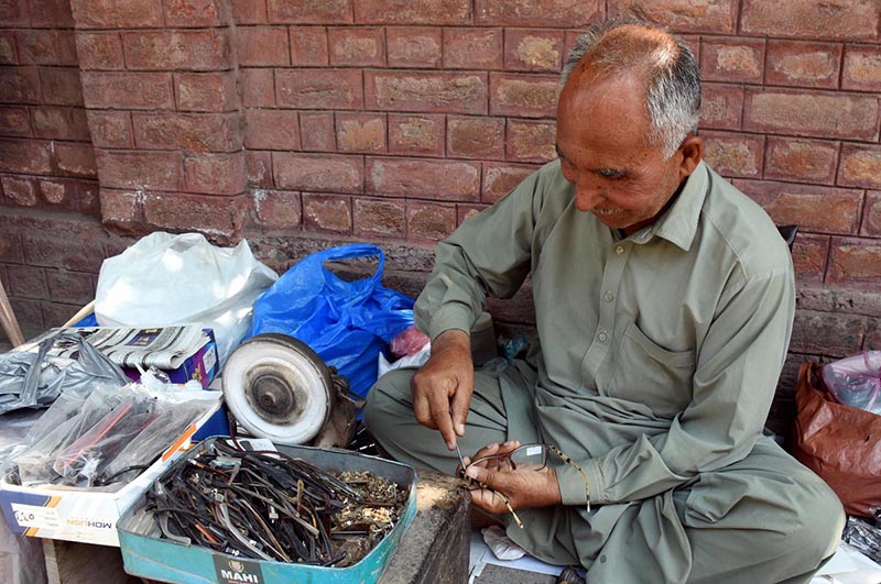 An artisan sits on the Mall Road footpath, repairing eyeglass frames to earn a livelihood for his children