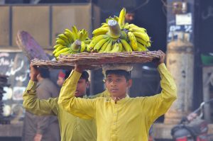 Young daily wage workers carry baskets of bananas on their heads for supply while the world observes International Labour Day