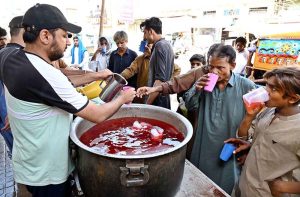 Members of the Hindu community distribute chilled summer drinks to the public outside Hindu Dharamshala on a hot day, offering relief to passersby in the city.