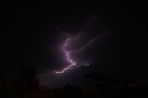A striking view of lightning flashing across the sky during rainfall, illuminating the dark clouds.