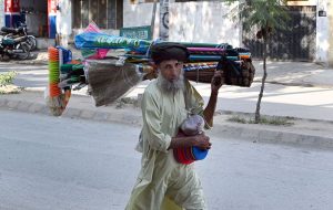 An elderly vendor carries household cleaning tools on his shoulder and walks along the roadside, offering them for sale