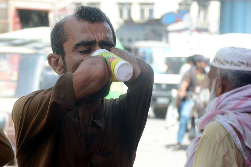 A disabled man drinks a sweet beverage from a volunteer-run camp set up during hot weather conditions