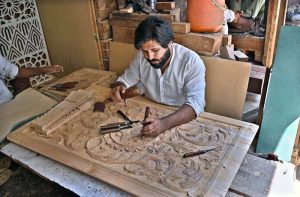 A carpenter busy in carving different designs on wooden sheet at his workplace.