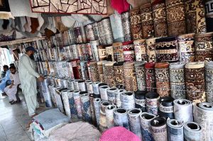A vendor arranges a vast collection of carpets and rugs of various designs, patterns and sizes at a carpet shop in weekly bazaar H-9, Federal Capital