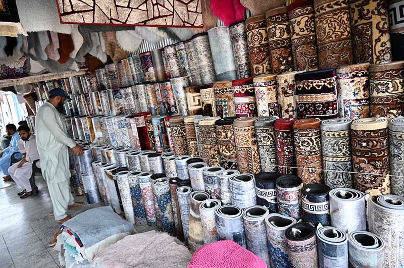 A vendor arranges a vast collection of carpets and rugs of various designs, patterns and sizes at a carpet shop in weekly bazaar H-9, Federal Capital