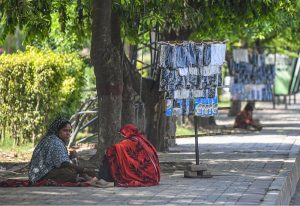 Women vendors take shelter in the shade of trees beside their roadside stall displaying socks and garments along a footpath in Murree Road, as the scorching summer heat forces street sellers to seek respite while waiting for customers.