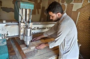 A carpenter busy in carving different designs on wooden sheet at his workplace.