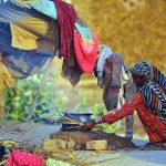 A woman cooks food for her family on a traditional earthen stove outside a temporary shelter in a rural settlement on the outskirts of the city
