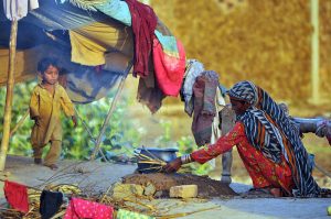 A woman cooks food for her family on a traditional earthen stove outside a temporary shelter in a rural settlement on the outskirts of the city
