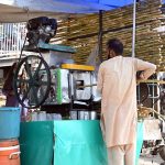 A vendor preparing and selling sugarcane juice at his roadside setup during hot weather in the Federal Capital