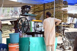 A vendor preparing and selling sugarcane juice at his roadside setup during hot weather in the Federal Capital