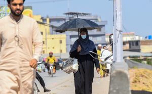 A woman shields herself from the scorching sun with an umbrella while walking along a busy road.