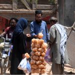 Customers purchase traditional snacks from a street vendor along a busy road near Gunj Mandi, as roadside food vendors continue to provide affordable snacks to residents despite the scorching summer heat