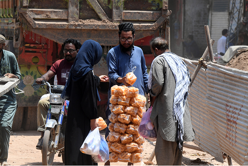 Customers purchase traditional snacks from a street vendor along a busy road near Gunj Mandi, as roadside food vendors continue to provide affordable snacks to residents despite the scorching summer heat