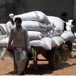 Labourers struggle to pull and push a heavily loaded cart piled high with sacks of goods through a dusty road near Gunj Mandi, reflecting the daily hardships faced by working-class people amid the scorching summer heat