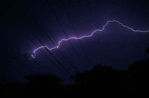 Lightning during rainfall illuminates the night sky, creating a spectacular scene over the city.