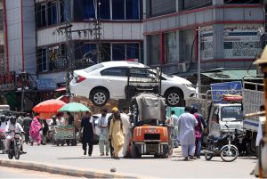 Labourers struggle to pull and push a heavily loaded cart piled high with sacks of goods through a dusty road near Gunj Mandi, reflecting the daily hardships faced by working-class people amid the scorching summer heat