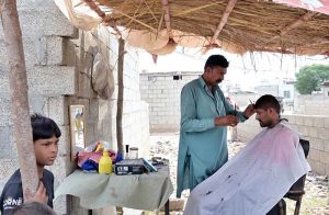 A barber is busy trimming the hair of a customer at a roadside setup.