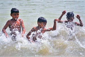 Children enjoy a refreshing swim and playing with water in the Pinyari Canal to escape the scorching summer heat in the city.
