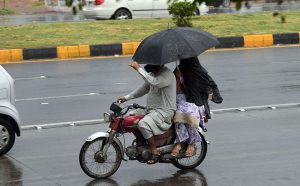 A family shields itself from a spell of heavy rain while riding a motorbike through the federal capital.