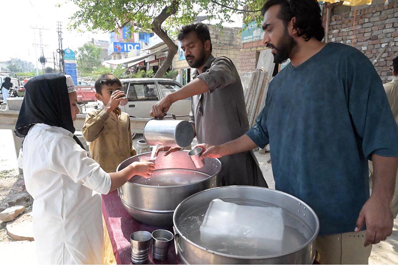 A volunteer serves free chilled drinks to passersby at a roadside stall during hot day at Lehtrar road in the Federal Capital