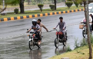 A family shields itself from a spell of heavy rain while riding a motorbike through the federal capital.
