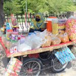 A woman vendor displays a variety of snacks and refreshments on her handcart to attract customers along General Bus Stand Road in the city