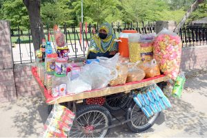 A woman vendor displays a variety of snacks and refreshments on her handcart to attract customers along General Bus Stand Road in the city