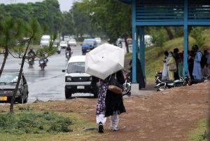 A family shields itself from a spell of heavy rain while riding a motorbike through the federal capital.