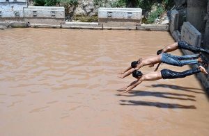 Young boys cool off by bathing in accumulated rainwater beneath the under-construction flyover at Katarian Bridge on I.J.P. Road, seeking relief from the summer heat.
