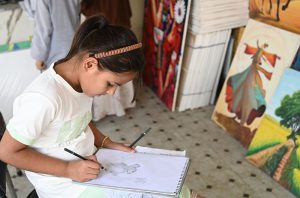 A girl draws a sketch following a step-by-step guide at a stall during the weekly bazaar held at Peshawar Mor, H-9, in the Federal Capital