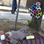 An elderly vendor enjoys a nap at roadside setup while selling balls at Peshawar Morr